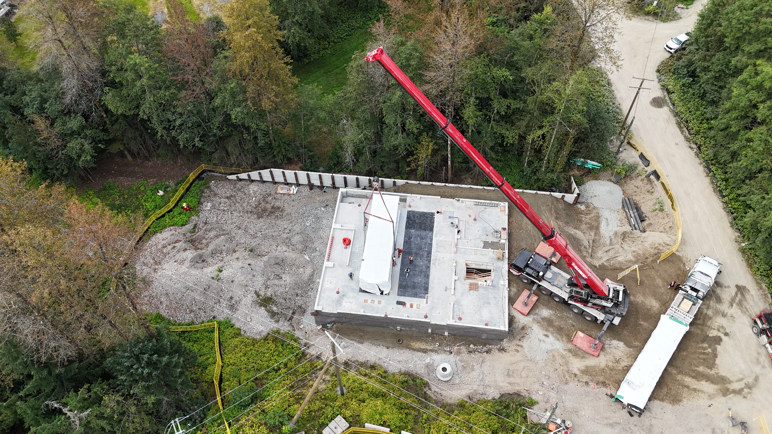 A crane lowers a white, rectangular shape onto a concrete foundation.
